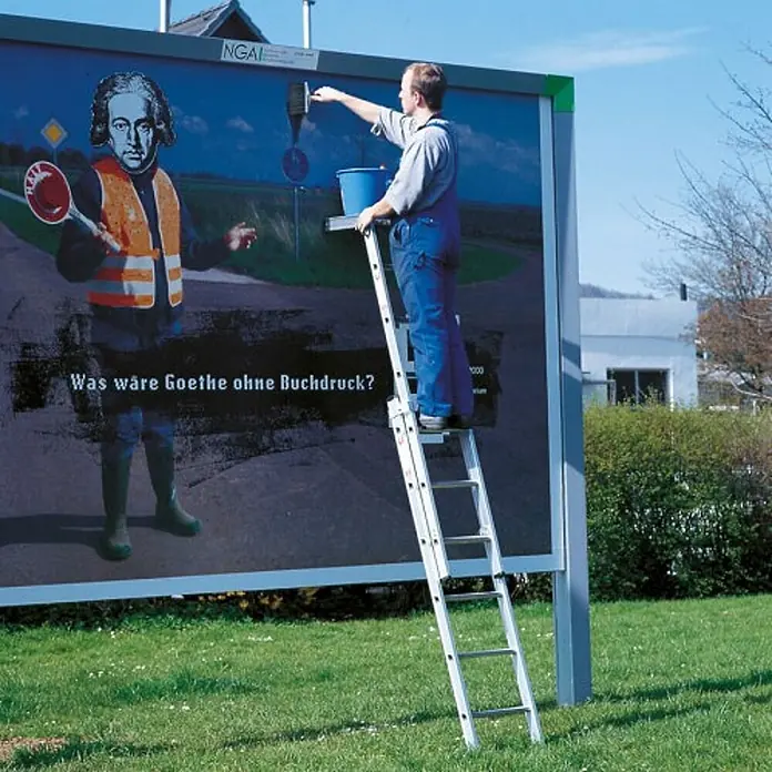 Euroline Mehrzweckleiter Premium 329 Plakatleiter 3x9 Sprossen - Anzahl Tritte: 9 Stk., Arbeitshöhe: 7.100 m, Aluminium - Silberne Aluminium-Mehrzweckleiter, von einem Mann auf einer Plakatwand verwendet.