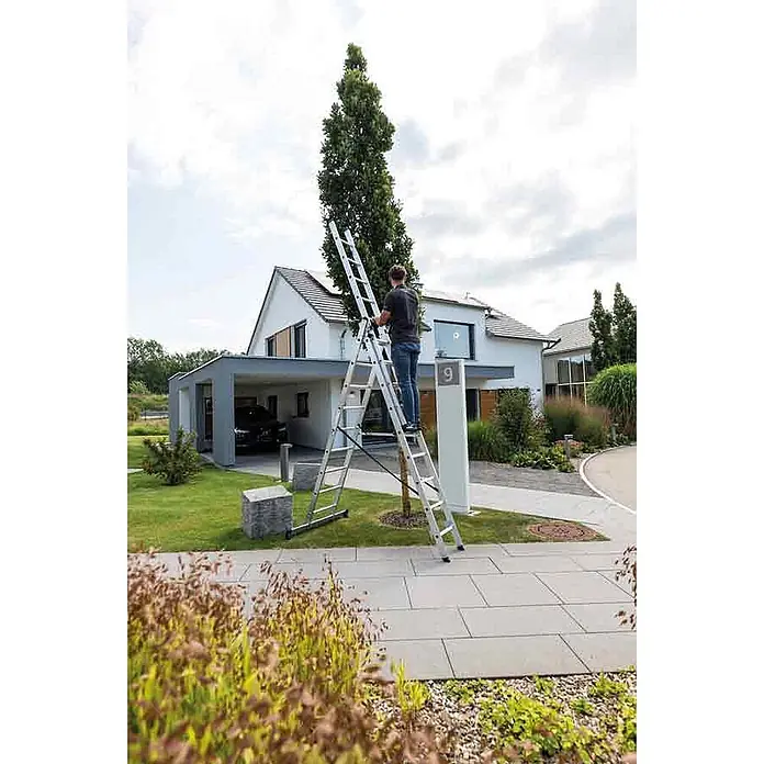 Munk Mehrzweckleiter Mehrzweckleiter mit Nivello® Traverse 3x8 Sprossen - Anzahl Tritte: 8 Stk., Arbeitshöhe: 6.900 m, Aluminium - Eine silberne Aluminium-Mehrzweckleiter, vollständig ausgezogen, unterstützt einen Mann bei der Arbeit im Freien nahe einem hohen Baum.