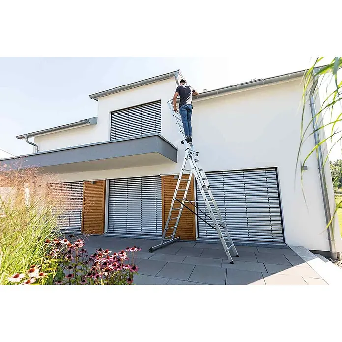 Munk Mehrzweckleiter Mehrzweckleiter mit Nivello® Traverse 3x8 Sprossen - Anzahl Tritte: 8 Stk., Arbeitshöhe: 6.900 m, Aluminium - Eine Aluminium-Mehrzweckleiter trägt einen Mann beim Reinigen der Dachrinne eines modernen weißen Hauses.