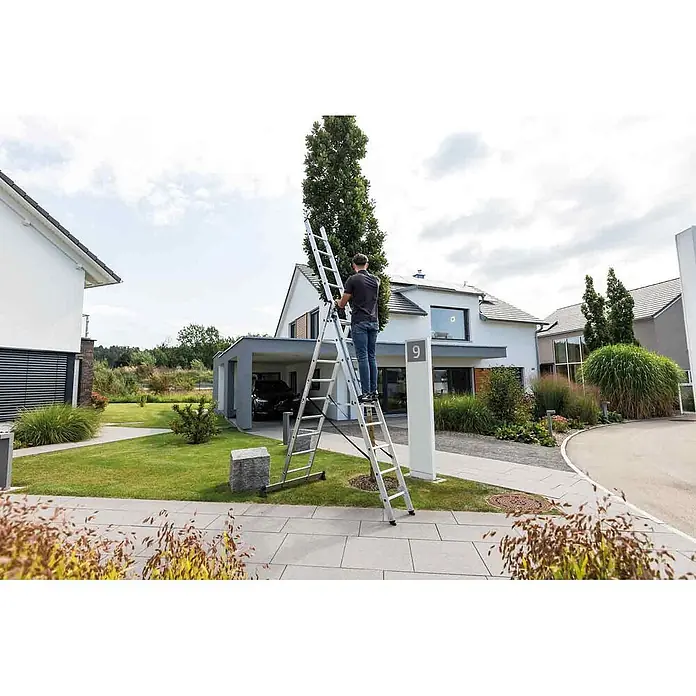 Munk Mehrzweckleiter Mehrzweckleiter mit Nivello® Traverse 3x8 Sprossen - Anzahl Tritte: 8 Stk., Arbeitshöhe: 6.900 m, Aluminium - Mann steht auf einer silbernen Aluminium-Mehrzweckleiter, die im Freien als Stehleiter aufgestellt ist.