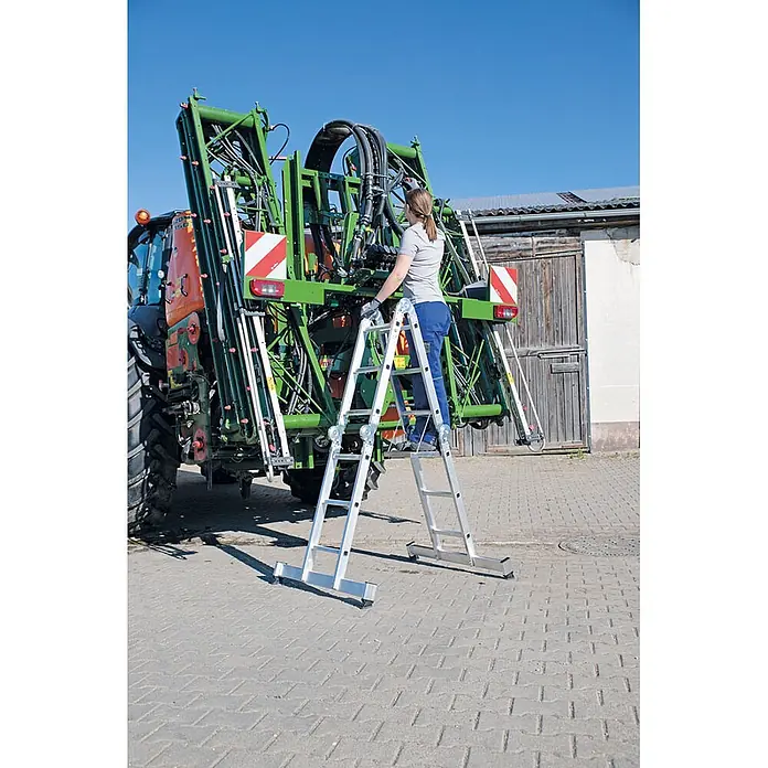 Munk Mehrzweckleiter Vielzweckleiter mit Nivello® Traverse 4x4 Sprossen - Anzahl Tritte: 4 Stk., Arbeitshöhe: 5.850 m, Aluminium - Silberne Mehrzweckleiter, von einer Frau zum Zugang zu einer großen Landmaschine verwendet.