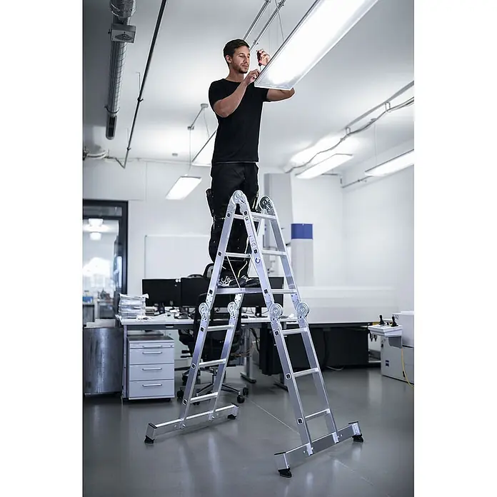 Munk Mehrzweckleiter Vielzweckleiter mit Nivello® Traverse 4x4 Sprossen - Anzahl Tritte: 4 Stk., Arbeitshöhe: 5.850 m, Aluminium - Mann auf einer silbernen Aluminium-Mehrzweckleiter arbeitet an einer Deckenleuchte.