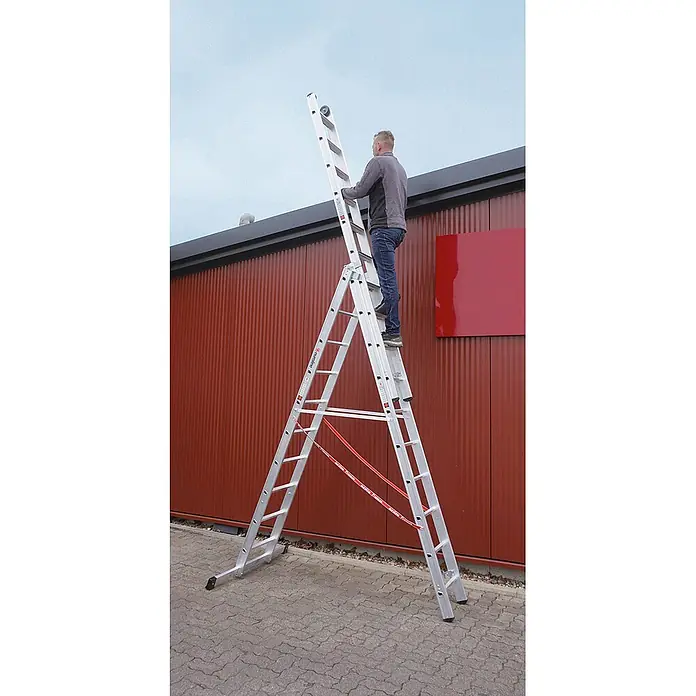 Euroline Mehrzweckleiter Premium 30777 Stufen Mehrzweckleiter mit Wandlaufrollen 3-teilig 3x8 Stufen - Anzahl Tritte: 8 Stk., Arbeitshöhe: 6.500 m, Belastbarkeit: 150 kg, Aluminium - Silberne Mehrzweckleiter, von einer Person zum Erreichen eines roten Gebäudedachs genutzt.