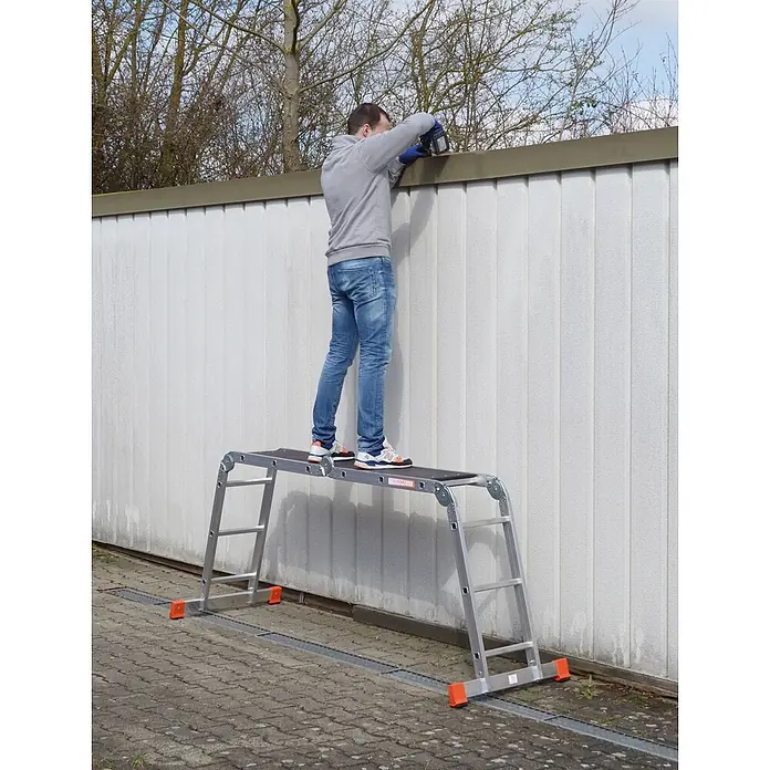 Siedra-Leitern Mehrzweckleiter Kofferraumleiter 985 4x3 Sprossen - Anzahl Tritte: 3 Stk., Arbeitshöhe: 3.600 m, Aluminium - Mann auf einer Aluminium-Arbeitsplattform mit dunkler Anti-Rutsch-Oberfläche, arbeitet an einer hohen Wand.