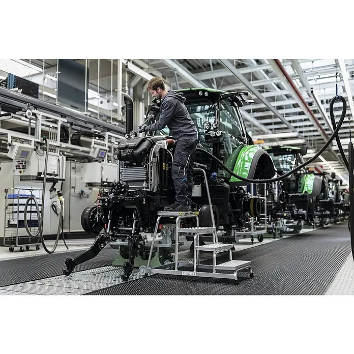 Munk Arbeitsplattform Arbeitspodest R13 starr 4 Stufen - Anzahl Tritte: 4 Stk., Arbeitshöhe: 2.800 m, Aluminium - Silberne, dreistufige mobile Arbeitsplattform, von einem Techniker zur Montage eines grünen Traktors genutzt.