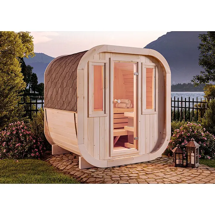 FinnTherm Fasssauna ScandiCube Mini XS - Holz, L x B x H: 166 x 21 x 214 cm - Hölzerne Fasssauna mit Schindeldach, im Freien an einem See mit Bergen im Hintergrund, was ein ruhiges Wellness-Erlebnis suggeriert.