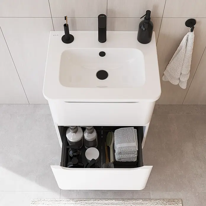 VitrA Integra Round Badmöbel-Set - Gesamtbreite Badmöbel: 60 cm, Weiß, Matt - Weißer Waschtisch mit integriertem Becken, schwarzem Wasserhahn und Zubehör. Die offene Schublade zeigt geordnete Toilettenartikel und betont den praktischen Stauraum.
