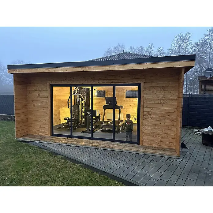 Fjordholz Gartenhaus - Außenmaß inkl. Dachüberstand (B x T): 597 x 465 cm, Holz, Grau Imprägnierung - Hölzernes Gartengymnastikhaus mit großen Glasschiebetüren, das Fitnessgeräte und ein Kind beherbergt, von außen in einem Garten gesehen.