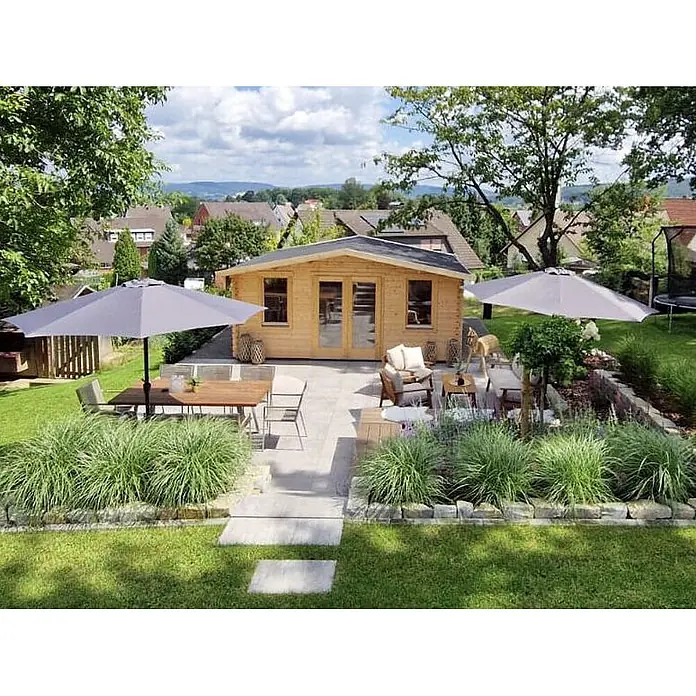 Fjordholz Gartenhaus Agnes 44 Farbbehandlung Lichtgrau - Außenmaß inkl. Dachüberstand (B x T): 500 x 400 cm, Holz, Naturbelassen - Helles Holzgartenhaus mit Glastüren, auf einer Terrasse mit Gartenmöbeln und Sonnenschirmen in einem Landschaftsgarten.