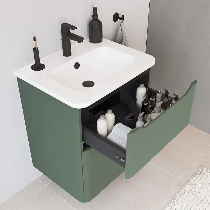 VitrA Integra Round Badmöbel-Set - Gesamtbreite Badmöbel: 60 cm, Moosgrün, Matt - Grüner Badmöbel mit weißem Waschbecken, schwarzem Wasserhahn. Geöffnete Schublade zeigt Toilettenartikel und weiße Handtücher.