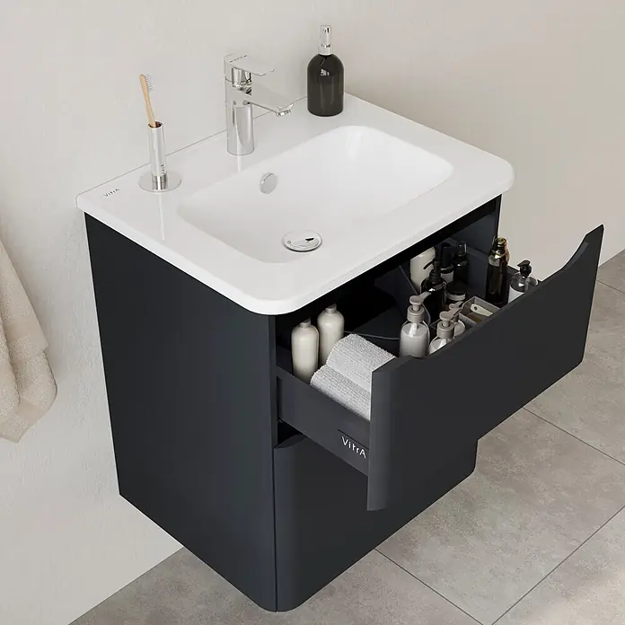 VitrA Integra Round Badmöbel-Set - Gesamtbreite Badmöbel: 60 cm, Graphit, Matt - Dunkelgrauer Badschrank mit weißem integriertem Waschbecken und offener Schublade, die Toilettenartikel und Handtücher zeigt.