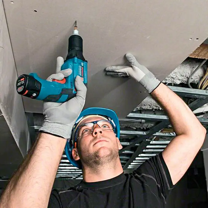 Bosch Professional Atornillador para placas de yeso de batería GTB 12V-11 - 12 V, 2 baterías, 2 Ah - Artesano usando un taladro atornillador inalámbrico Bosch para fijar paneles de yeso al techo.