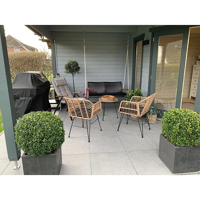 Fjordholz Gartenhaus Nora 44 H Modern - Außenmaß inkl. Dachüberstand (B x T): 740 x 320 cm, Holz, Farbbehandlung Lichtgrau - Zwei hellbraune Rattan-Gartenstühle mit schwarzen Beinen und ein Glastisch auf einer grauen Terrasse bilden eine gemütliche Sitzecke.