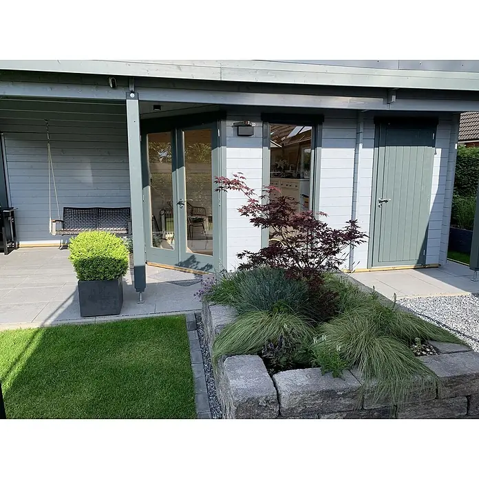 Fjordholz Gartenhaus Nora 44 H Modern - Außenmaß inkl. Dachüberstand (B x T): 740 x 320 cm, Holz, Farbbehandlung Lichtgrau - Moderner grauer Gartenpavillon mit Glastüren und überdachter Terrasse, eingebettet in eine Landschaftsgestaltung.