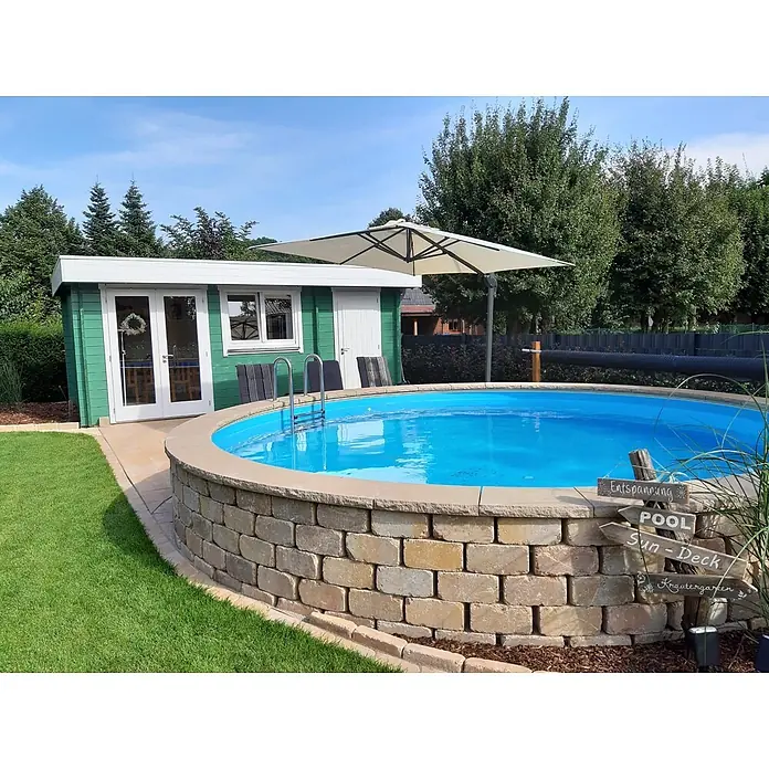 Fjordholz Gartenhaus Kurt 44 D Farblose Imprägnierung - Außenmaß inkl. Dachüberstand (B x T): 578 x 400 cm, Holz, Naturbelassen - Ein Aufstellpool mit Steinmauerumrandung in einem sonnigen Garten, neben einem grünen Gartenhaus und einem Sonnenschirm.