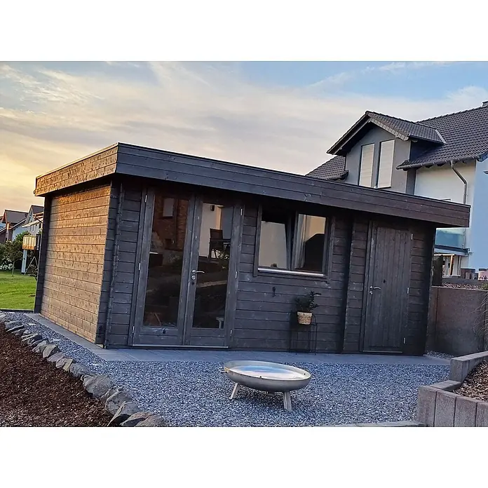 Fjordholz Gartenhaus Kurt 44 D Farblose Imprägnierung - Außenmaß inkl. Dachüberstand (B x T): 578 x 400 cm, Holz, Naturbelassen - Dunkles Holz-Gartenhaus mit Glastüren, Fenster und einer Feuerschale auf einer Kiesfläche.