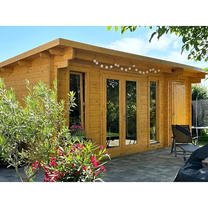 Fjordholz Gartenhaus Jacob 44 C mit Abstellraum - Außenmaß inkl. Dachüberstand (B x T): 570 x 360 cm, Holz, Kiefer/Pinie Imprägnierung - Ein hellbraunes Gartenhaus aus Holz mit Glastüren, Flachdach und Lichterkette auf einer gepflasterten Terrasse im Garten.