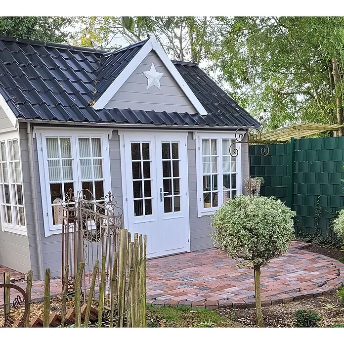 Fjordholz Gartenhaus Teehaus Windsor 44 Farbbehandlung Carbongrau - Außenmaß inkl. Dachüberstand (B x T): 420 x 319,3 cm, Holz, Naturbelassen - Ein hellgrauer Gartenpavillon mit schwarzem Wellblechdach, weißen Fenstern und Türen und einem weißen Stern am Giebel, auf einer Ziegelterrasse.