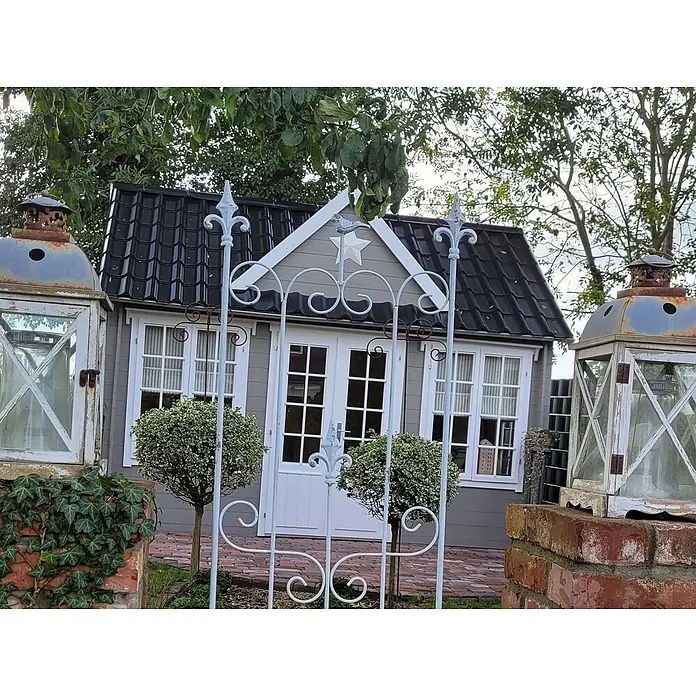 Fjordholz Gartenhaus Teehaus Windsor 44 Farbbehandlung Carbongrau - Außenmaß inkl. Dachüberstand (B x T): 420 x 319,3 cm, Holz, Naturbelassen - Ein charmantes graues Gartenhaus mit schwarzem Dach, weißer Verkleidung und einem verzierten weißen Tor davor, flankiert von dekorativen Laternen.