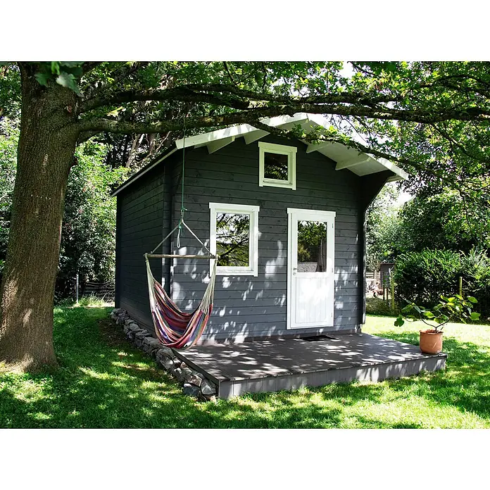 Fjordholz Gartenhaus Sönke 44 B - Außenmaß inkl. Dachüberstand (B x T): 388 x 488 cm, Holz, ohne Imprägnierung - Kleiner dunkelgrauer Holzschuppen mit weißer Verkleidung, bunter Hängesessel und Terrasse, umgeben von Bäumen und Gras.