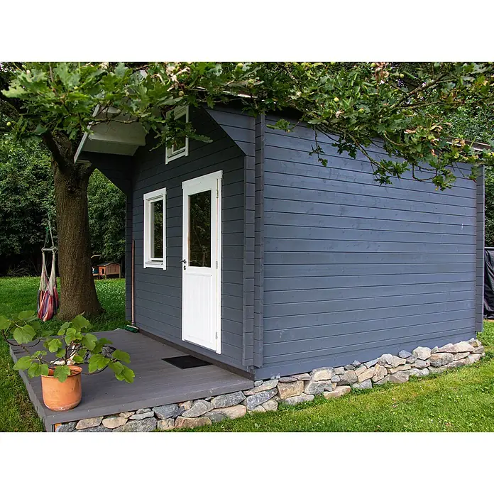 Fjordholz Gartenhaus Sönke 44 B - Außenmaß inkl. Dachüberstand (B x T): 388 x 488 cm, Holz, ohne Imprägnierung - Dunkelgraues Gartenhaus aus Holz mit weißen Fenstern und Tür, auf einer Terrasse in grünem Gras und Bäumen gelegen.