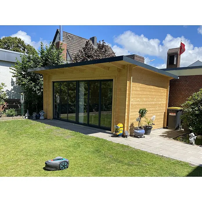 Fjordholz Gartenhaus Starla 44 E - Außenmaß inkl. Dachüberstand (B x T): 620 x 325 cm, Holz, Grau Imprägnierung - Ein modernes Gartenhaus aus Holz mit großen Glastüren steht in einem grünen Garten und bietet einen Wohnbereich im Freien.