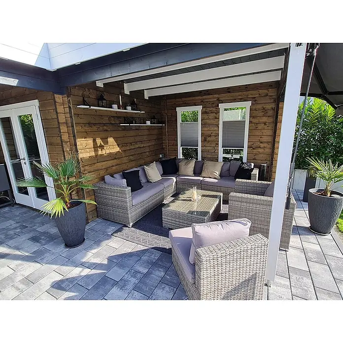 Fjordholz Gartenhaus Fred 44 Grau Imprägnierung - Außenmaß inkl. Dachüberstand (B x T): 573,2 x 573,2 cm, Holz, Naturbelassen - Graues Polyrattan-Loungeset mit hellen Kissen und Glas-Couchtisch auf gepflasterter Terrasse unter Holzpergola.