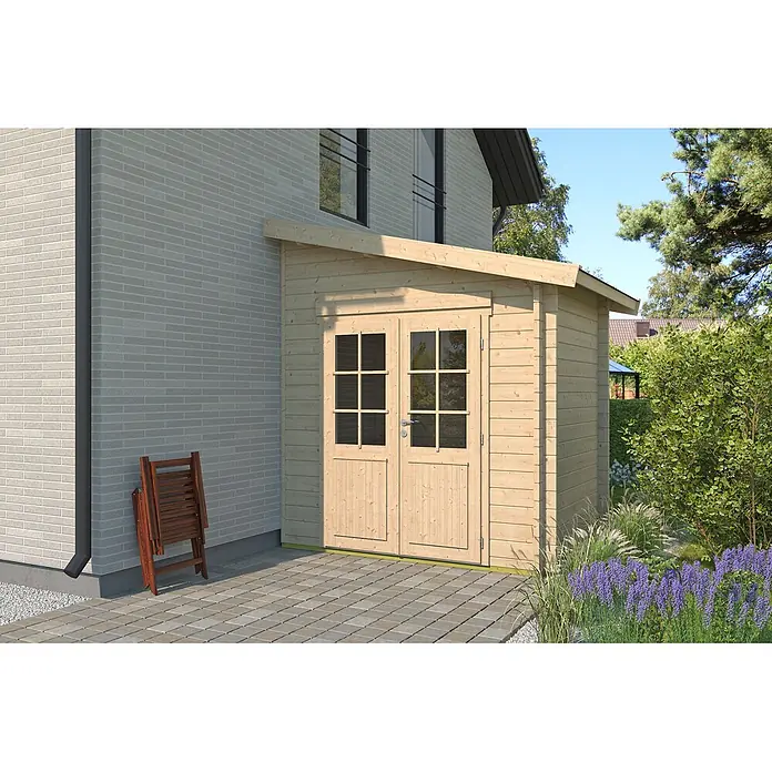 Fjordholz Gartenhaus Pulti 44 D - Außenmaß inkl. Dachüberstand (B x T): 250 x 200 cm, Holz, Naturbelassen - Heller Holzgeräteschuppen mit verglasten Doppeltüren, neben einem Ziegelhaus auf Pflastersteinen mit Gartenpflanzen.
