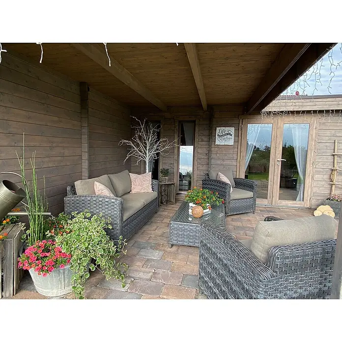 Fjordholz Gartenhaus Luisa 44 - Außenmaß inkl. Dachüberstand (B x T): 680 x 480 cm, Holz, Naturbelassen - Geflecht-Loungemöbel-Set für den Außenbereich mit grauen Kissen auf einer Terrasse.