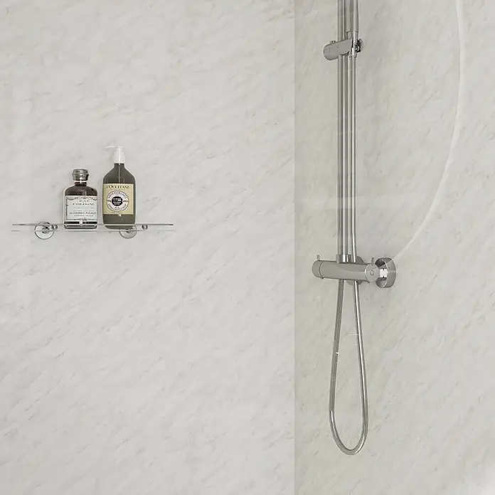 Wetwall Wandpaneel Elite - 16 x 242 cm, Carrara Marble, Abgerundete Kante - Modernes Duschsystem aus Chrom und helle Marmorwandpaneele in einer Badezimmerecke, mit einem Regal für Pflegeprodukte.