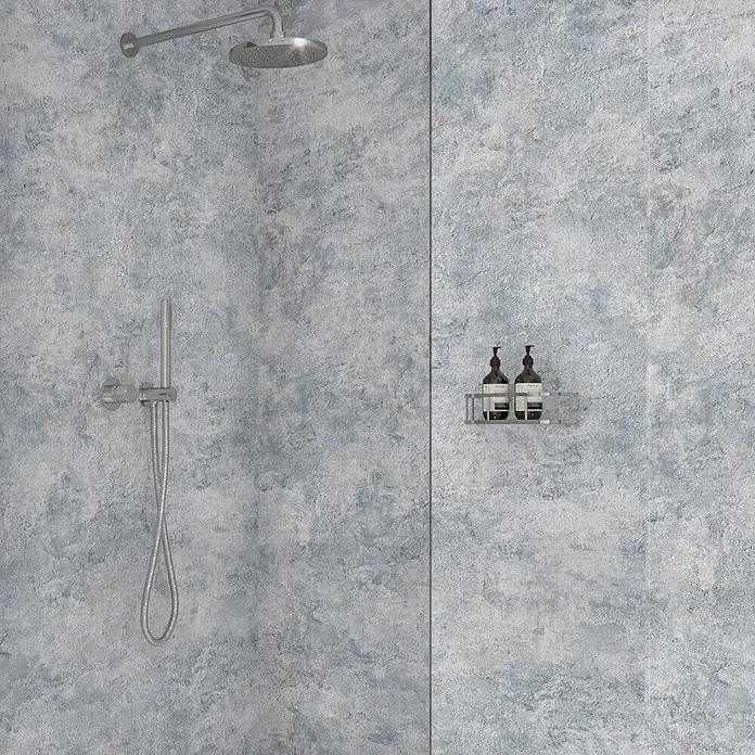 Wetwall Wandpaneel Elite - 16 x 242 cm, Caliza, Abgerundete Kante - Verchromte Duscharmaturen mit Kopfbrause, Handbrause und Ablagekorb mit Flaschen, an einer strukturierten blau-grauen Duschwand.