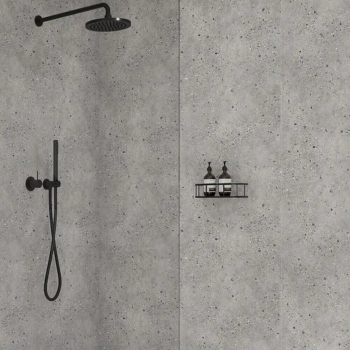 Wetwall Wandpaneel Elite - 16 x 242 cm, Pewter Terrazzo, Abgerundete Kante - Schwarzes mattes Duschsystem mit Kopf- und Handbrause und einem Ablagekorb mit zwei Flaschen an gesprenkelter grauer Wand.