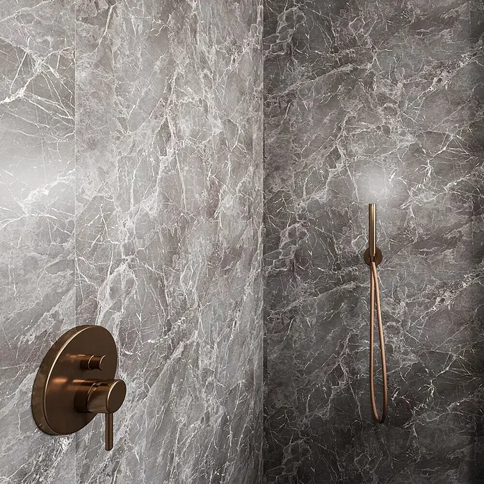 Wetwall Wandpaneel Elite - 16 x 242 cm, Welsh Slate, Abgerundete Kante - Bronzene Duscharmatur und Handbrause-Set an dunklen grauen Marmorfliesen in einem modernen Bad.