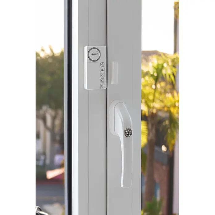 Abus Alarmanlage Time2Close Window Countdown Alarm - Weiß, 15 x 43 x 85 mm - Weißer ABUS Fensteralarm und weißer abschließbarer Fenstergriff an weißem Fensterrahmen.