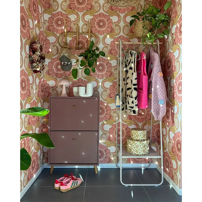 Schildmeyer Bjarne Schuhschrank - L x B x H: 19,5 x 59,8 x 92,2 cm, Mauve, Anzahl Fächer: 2 Stk. - Eine retrogestaltete Zimmerecke mit einem rosa Schuhschrank und einem weißen Kleiderständer, geschmückt mit Pflanzen und bunten Kleidungsstücken.