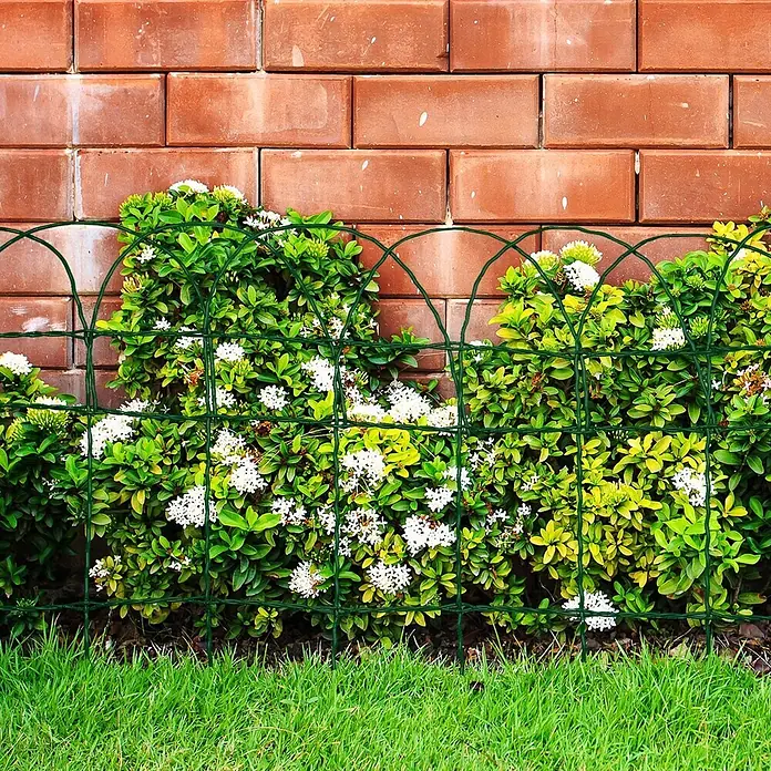 Floordirekt Maschendrahtzaun - 100 x 40 cm, Grün, Drahtstärke: 2,4 mm - 3 mm - Grüner Drahtgartenzaun mit Bogenmuster, begrenzt weiß blühende Büsche vor einer Ziegelmauer.