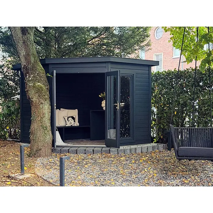 Fjordholz Gartenhaus Abbie 28 - Außenmaß inkl. Dachüberstand (B x T): 280 x 280 cm, Holz, Naturbelassen - Dunkelgraues Gartenhaus oder Outdoor-Büro mit offenen Türen, mit Bank und Kissen ausgestattet, in einem Garten.
