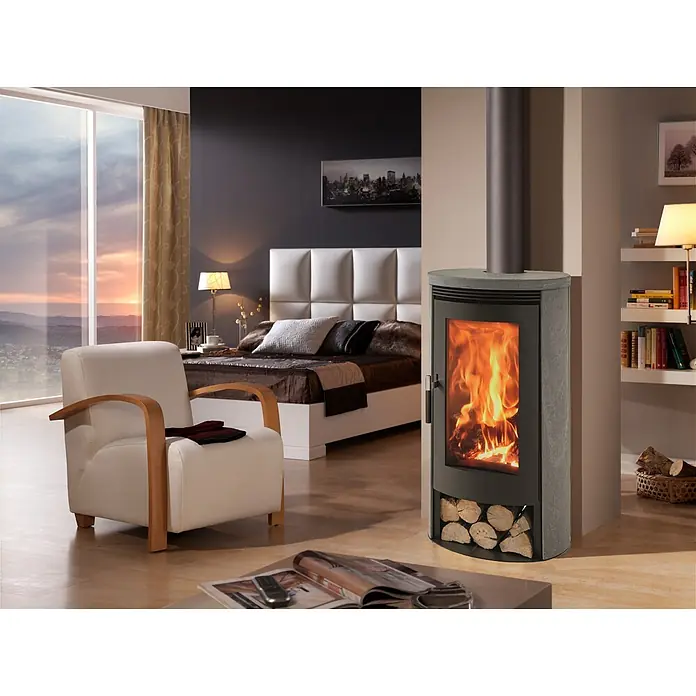 Panadero Kaminofen Baia Soap Ecodesign - 8 kW, Raumheizvermögen: 240 m³, Material Verkleidung: Stahl, Schwarz Metallic, Wirkungsgrad: 80,7 % - Moderner Holzofen mit grauer Steinplatte, brennende Holzscheite hinter Glastür und integriertem Holzlager, erwärmt ein gemütliches Zimmer.