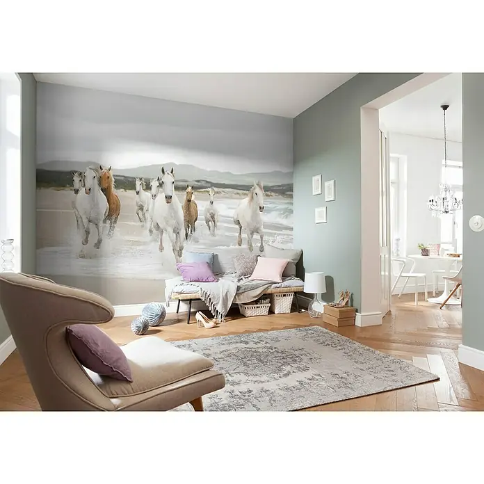 Komar Fototapete White Horse - 8 -tlg., B x H: 368 x 254 cm, Papier - Elegantes Interieur mit einem auffälligen Wandbild von galoppierenden Pferden am Strand, akzentuiert durch einen stilvollen Sessel und einen dekorativen Teppich.