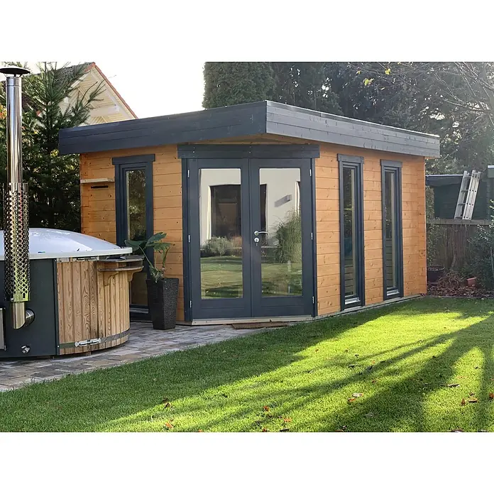 Fjordholz Gartenhaus Birger 44 - Außenmaß inkl. Dachüberstand (B x T): 448 x 298 cm, Holz, ohne Imprägnierung - Helles Gartenhaus aus Holz mit dunkelgrauen Rahmen und Flachdach, im grünen Garten neben einem Whirlpool mit Schornstein.