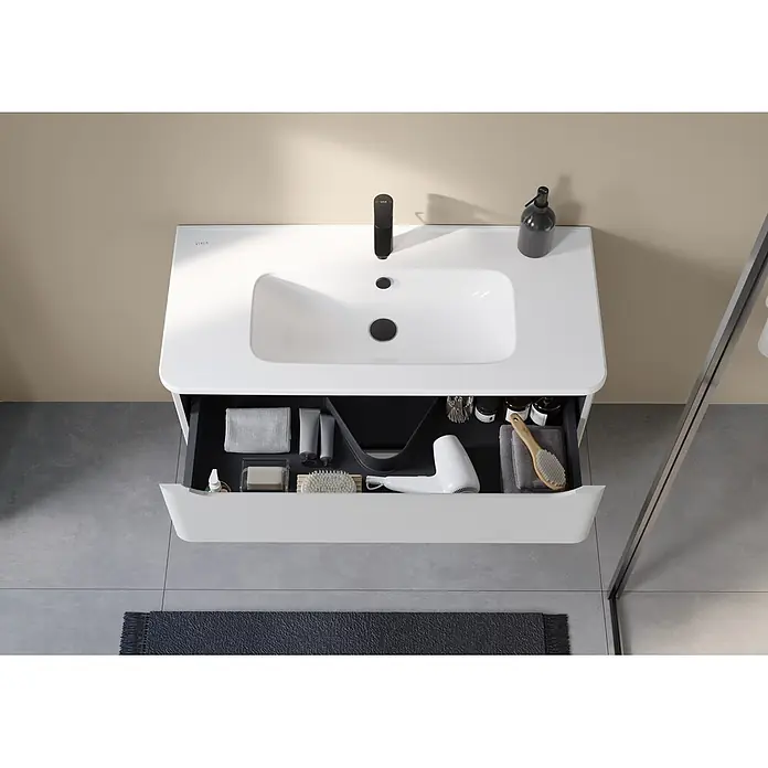 VitrA Integra Round Badmöbel-Set - Gesamtbreite Badmöbel: 100 cm, Hellgrau, Matt - Weißer Waschtisch mit integriertem Waschbecken und schwarzem Wasserhahn, offene Schublade mit Badutensilien. Draufsicht im modernen Badezimmer.
