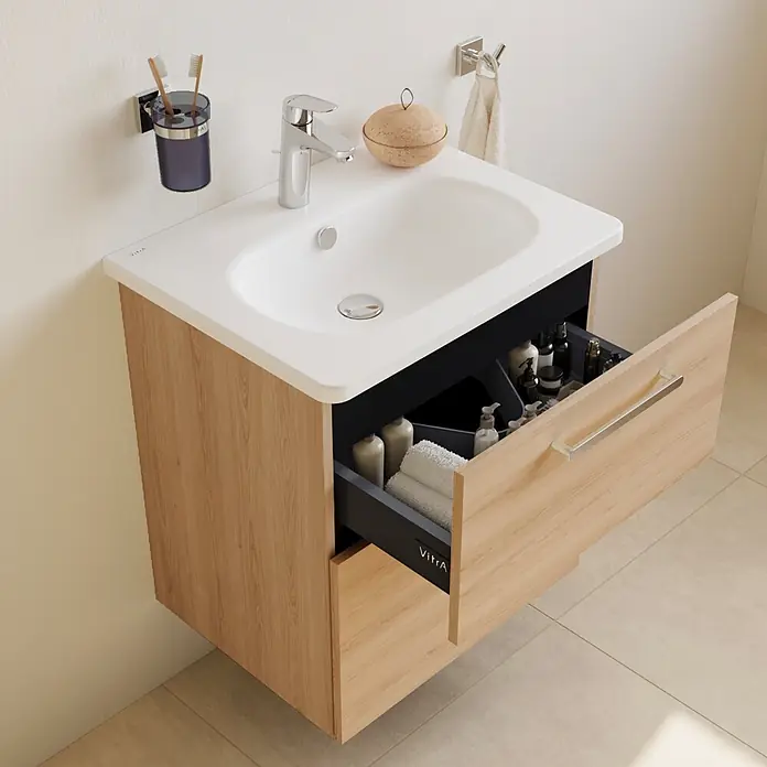 VitrA Badmöbel-Set Root Flat - Gesamtbreite Badmöbel: 60 cm, Eiche Natur - Wandhängender Badunterschrank in heller Holzoptik mit weißem Waschbecken und offener schwarzer Schublade voller Badezimmerartikel.