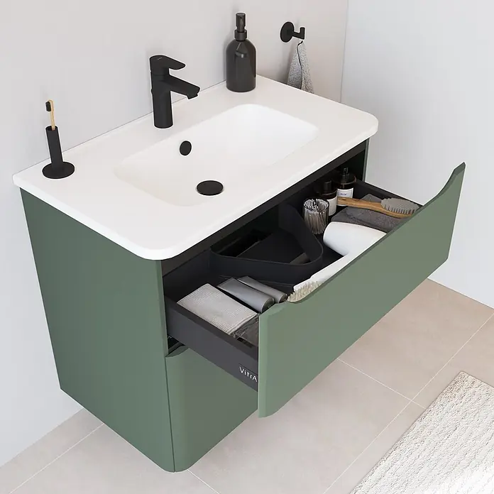VitrA Integra Round Badmöbel-Set - Gesamtbreite Badmöbel: 80 cm, Moosgrün, Matt - Wandmontierter salbeigrüner Badunterschrank mit weißem Waschbecken, schwarzem Wasserhahn und geöffneter Schublade mit Toilettenartikeln.