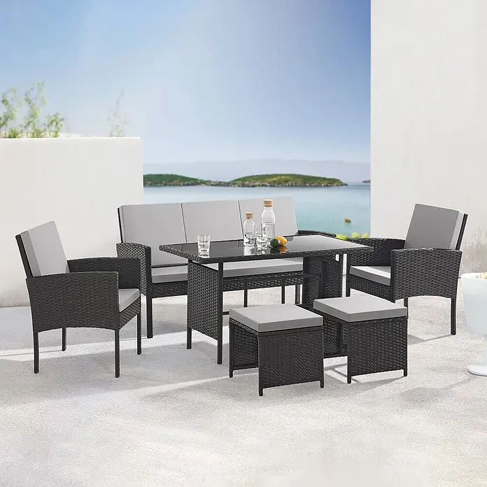 SVITA Gartenmöbel-Set DENVER - 6 -tlg., Polyrattan - Dunkelgraues Rattan-Gartenset mit Tisch, Sofa, zwei Sesseln und zwei Hockern, alle mit hellgrauen Kissen, auf einer Terrasse am Meer.