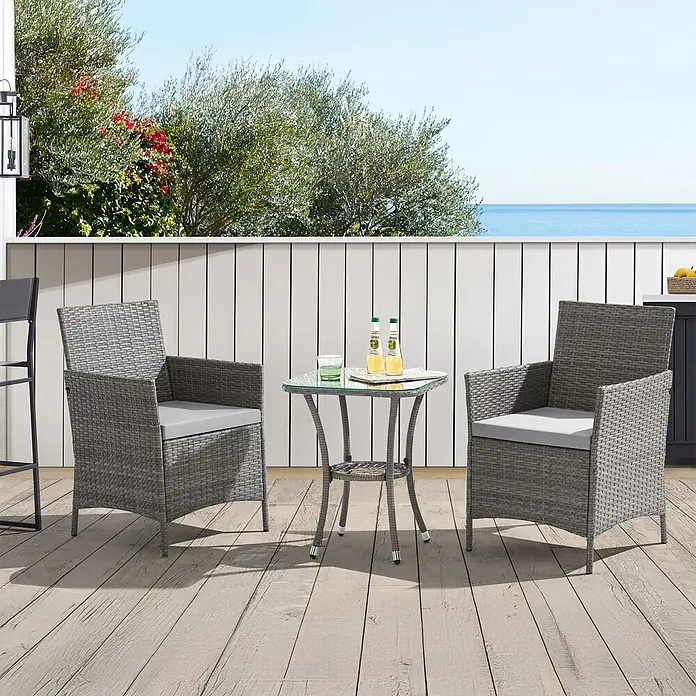 SVITA Loungemöbel-Set - 3 -tlg., Polyrattan, Grau - Graues Rattan-Terrassenset mit zwei Stühlen und einem Tisch mit Glasplatte auf einer Holzterrasse mit Meerblick.