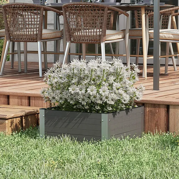 Outsunny Hochbeet - Aluminium, Grau - Dunkelgrauer Verbundstoff-Pflanzkasten mit weißen margeritenähnlichen Blumen, auf Gras neben einer Holzterrasse.