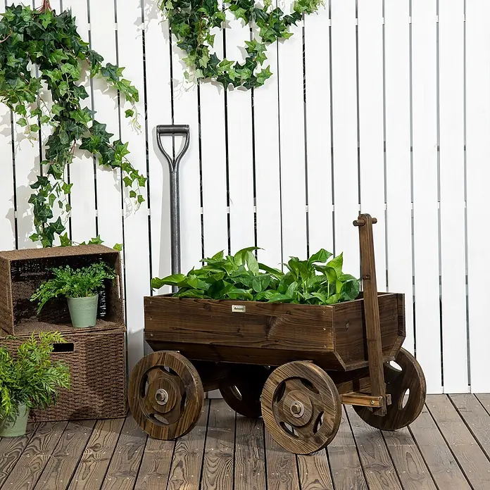 Outsunny Hochbeet - Holz, Verkohlt - Dunkelbrauner Holzwagen-Pflanzkübel mit vier Rädern, gefüllt mit Grünpflanzen, auf einer Holzterrasse in Gartenumgebung.