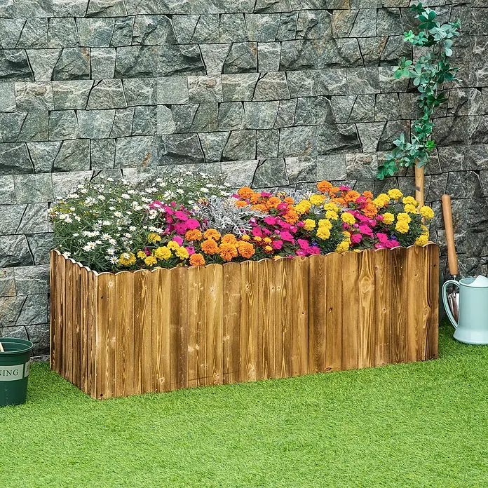 Furnicato Hochbeet - 120 x 40 x 40 cm, Holz, Naturholz - Rustikales braunes Hochbeet aus Holz mit gewelltem Rand, gefüllt mit bunten Blumen auf Kunstrasen vor einer Steinwand.