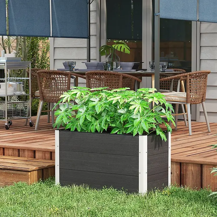 Outsunny Hochbeet - 100 x 50 x 55,5 cm, Aluminium, Grau - Ein rechteckiger dunkelgrauer Outdoor-Pflanzkübel mit weißen Ecken, gefüllt mit grünen Pflanzen, steht auf Gras neben einer Holzterrasse.