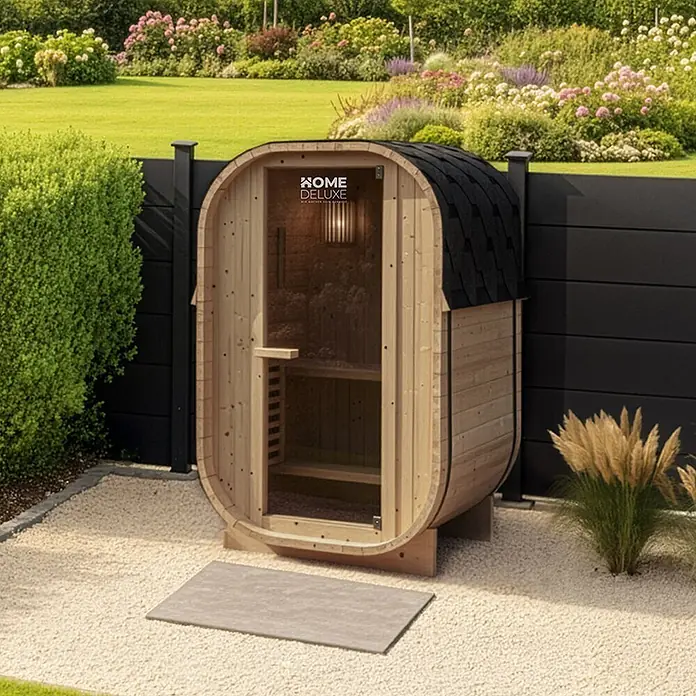 Home Deluxe Fasssauna CUBE S - Elektroofen, Holz - Outdoor-Fasssauna aus hellem Holz mit schwarzem Schindeldach und Glastür.